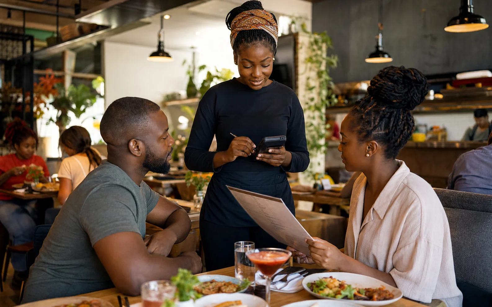 Restaurant server entering an order on a handheld device beside two seated diners